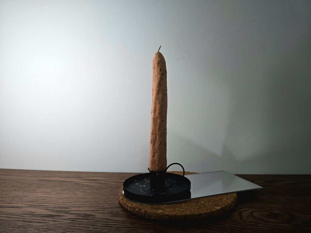 Tall brown candle on a black stand with a white wall background