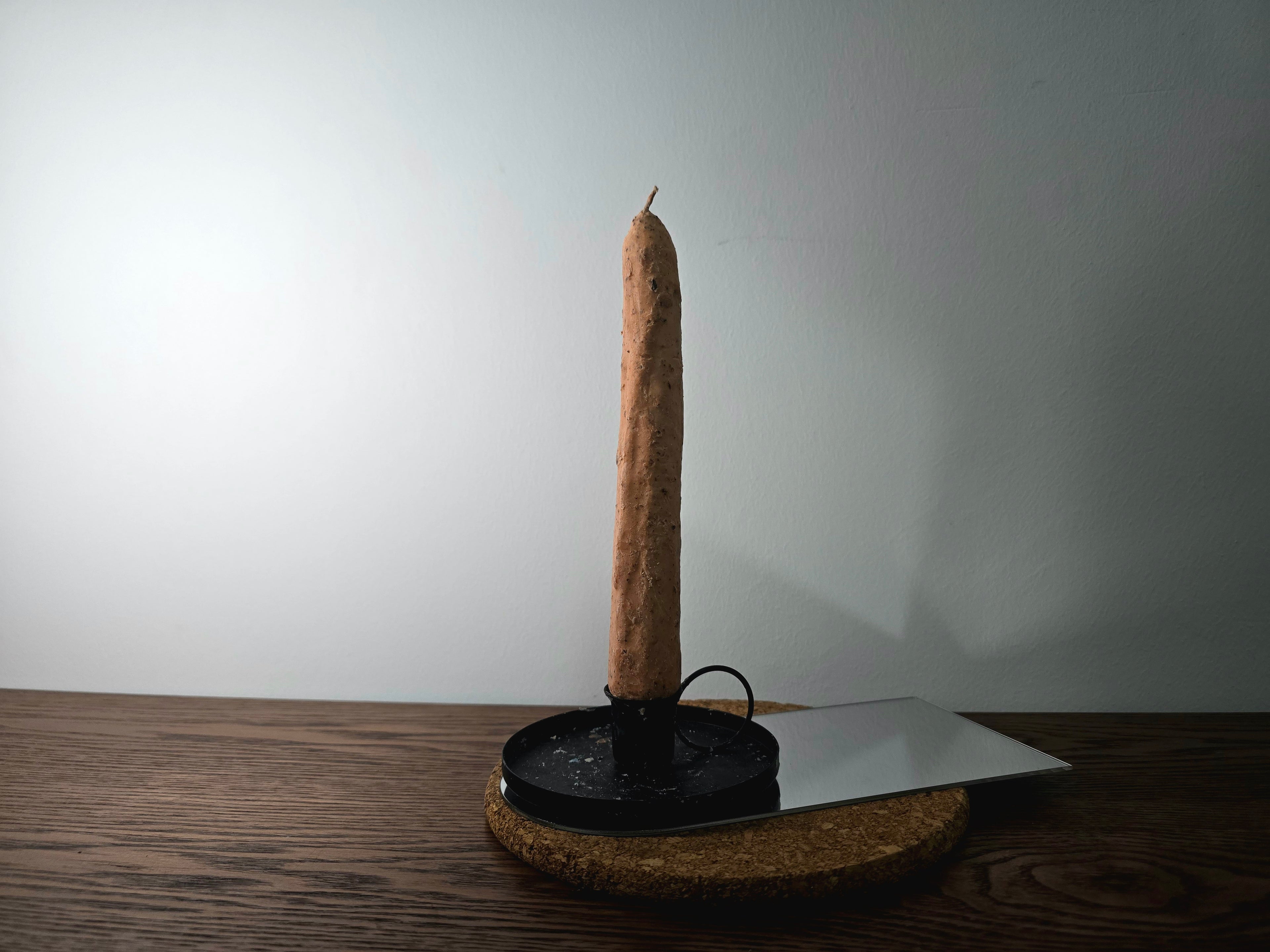 Tall brown candle on a black stand with a white wall background