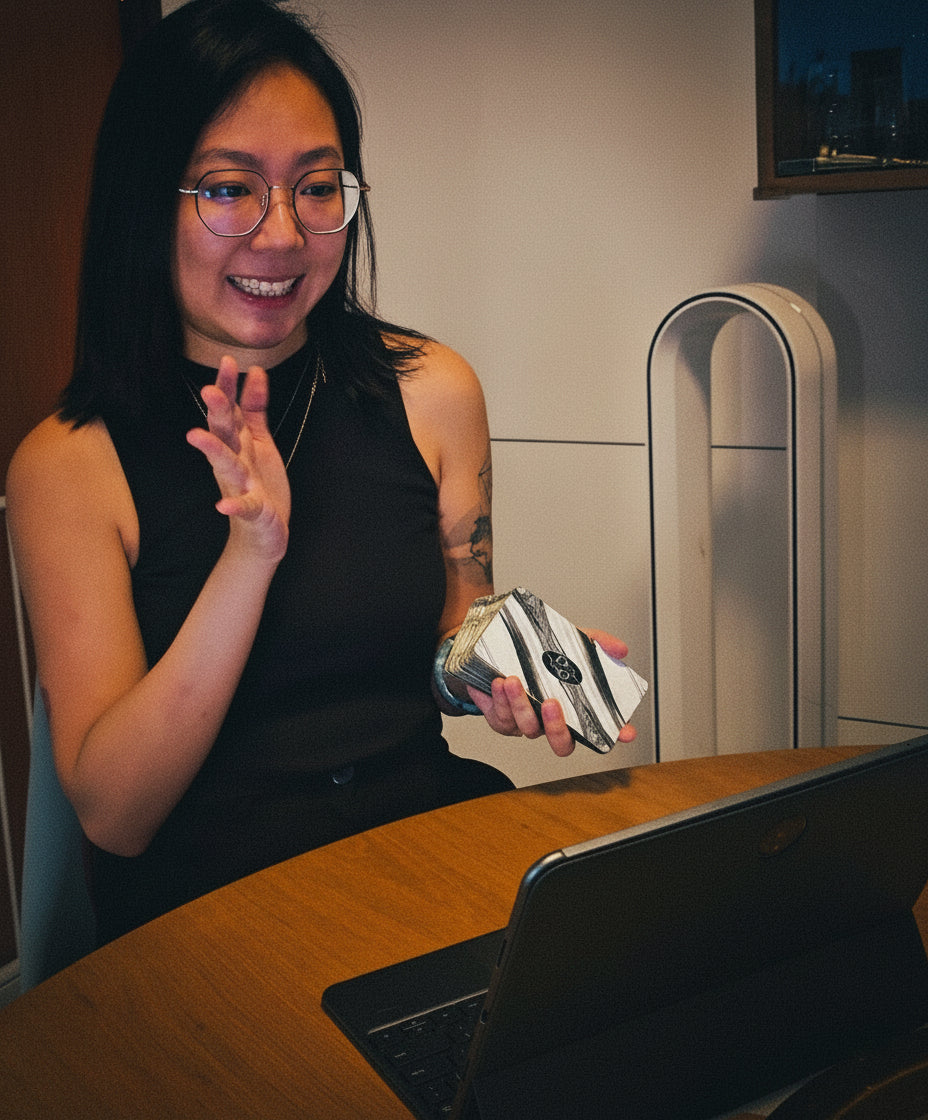 Person sitting at a table with a laptop, performing tarot reading.