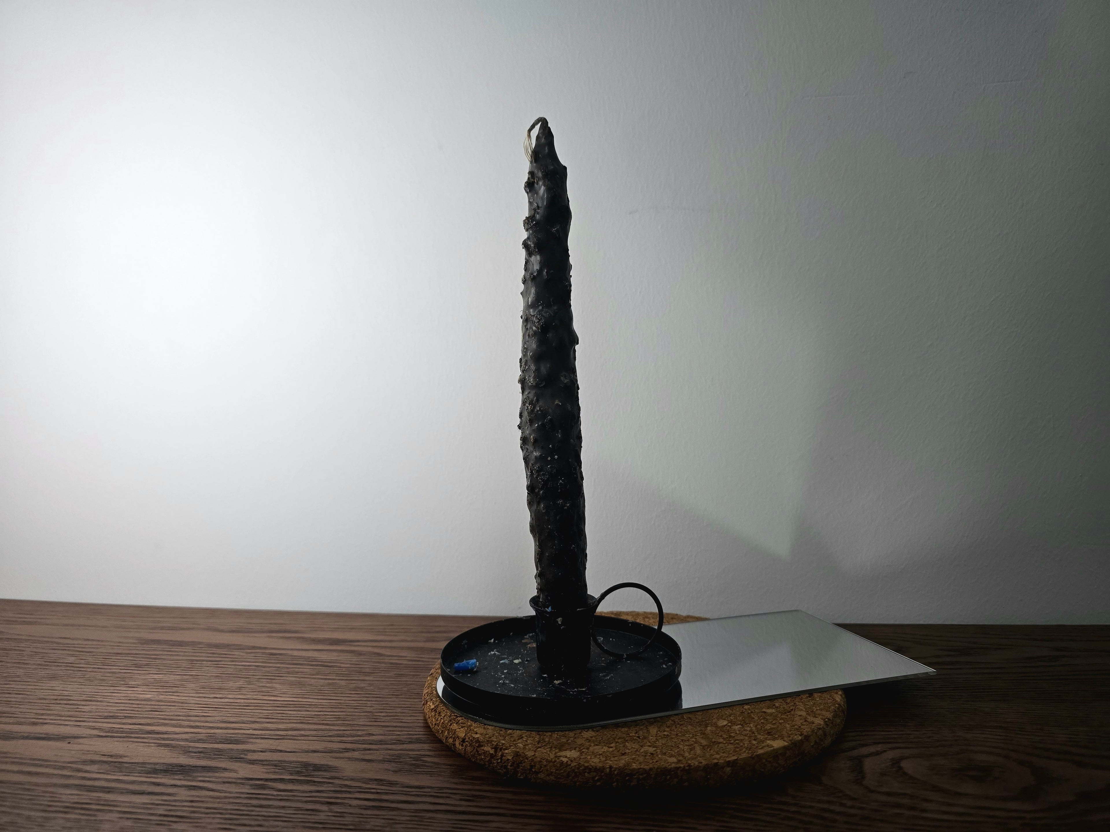 Black candle-like object on a wooden base against a white wall