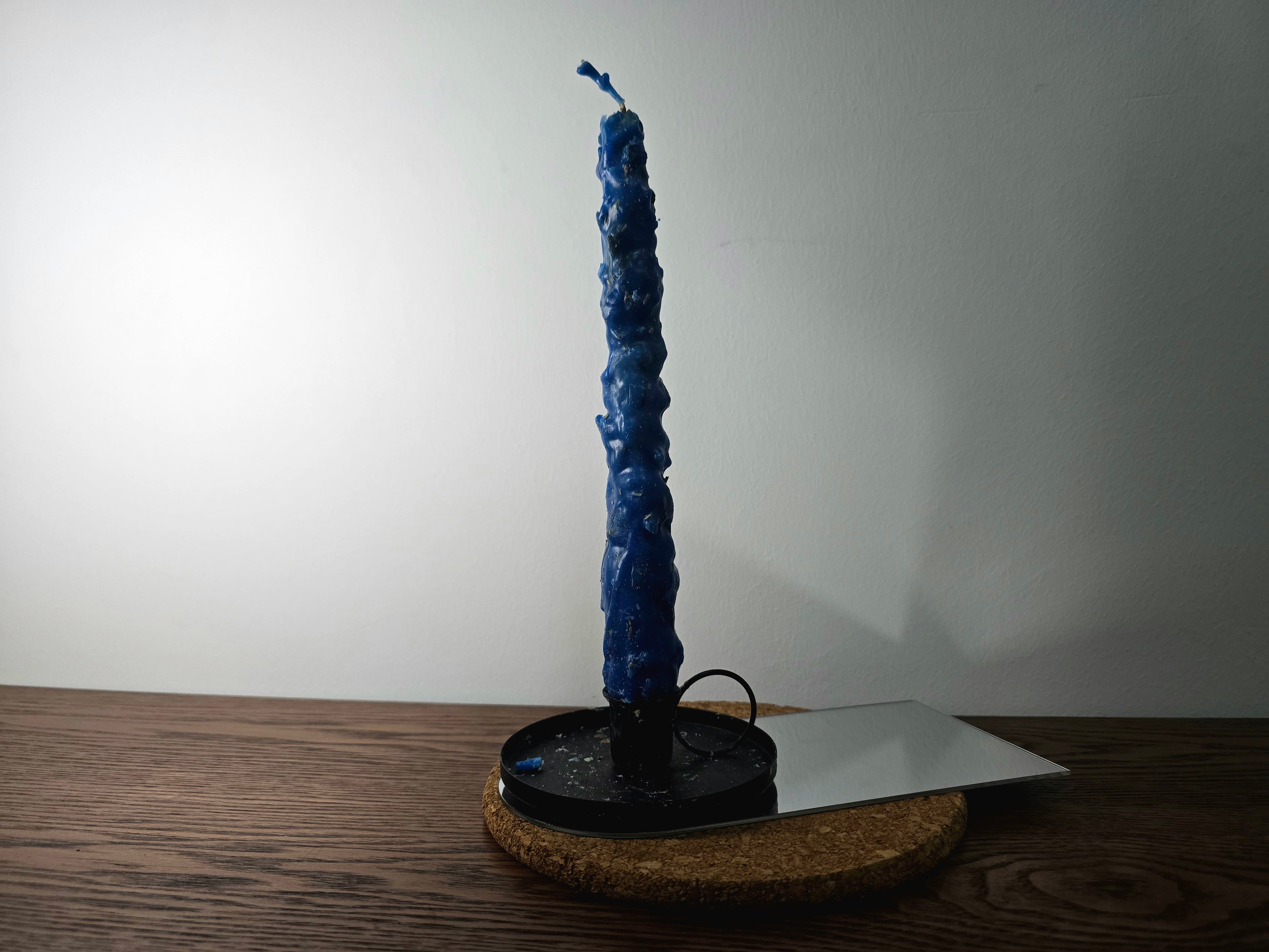 Blue textured candle on a black stand against a white wall