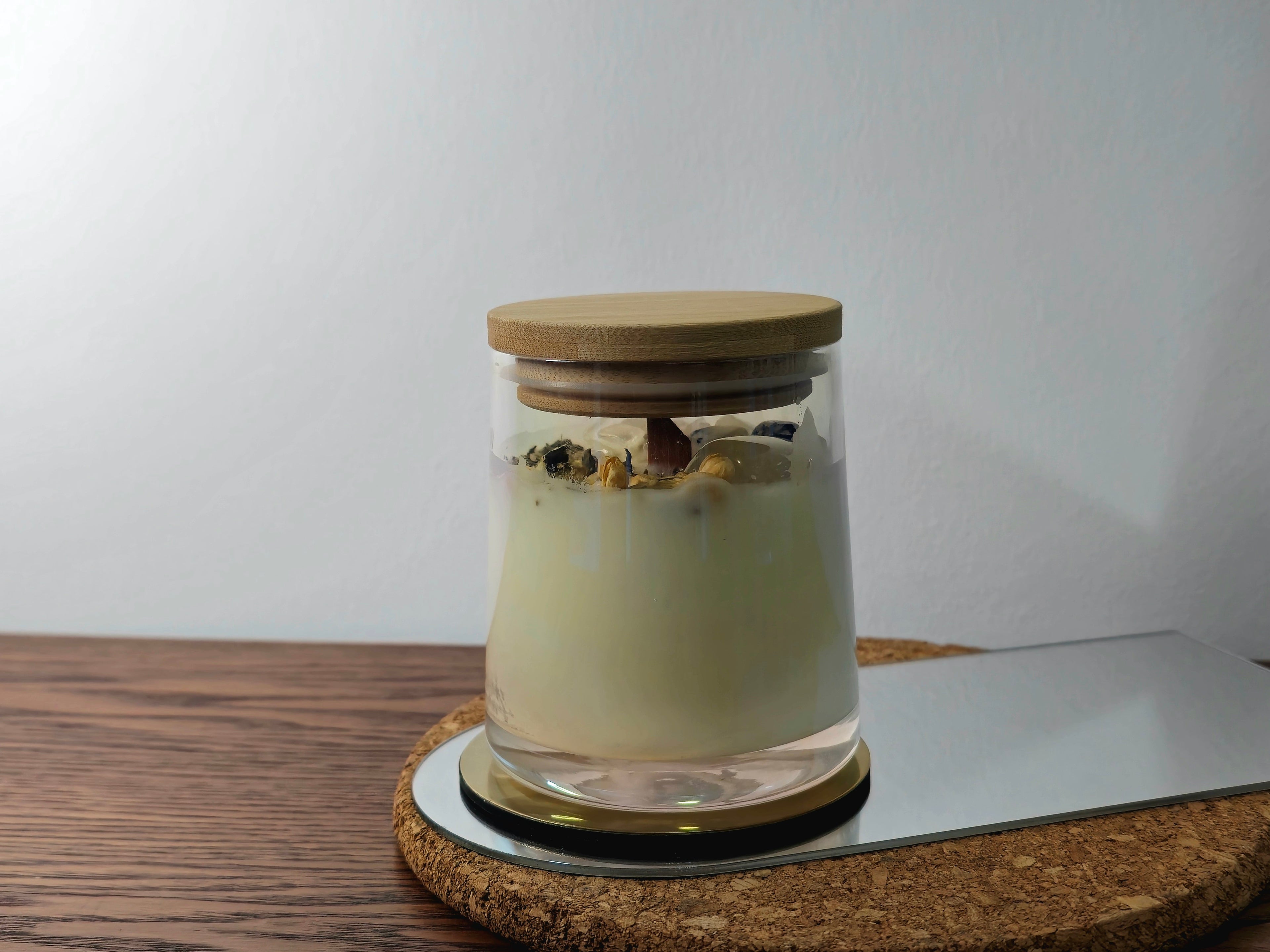 Glass jar with wooden lid on a cork coaster with a white background
